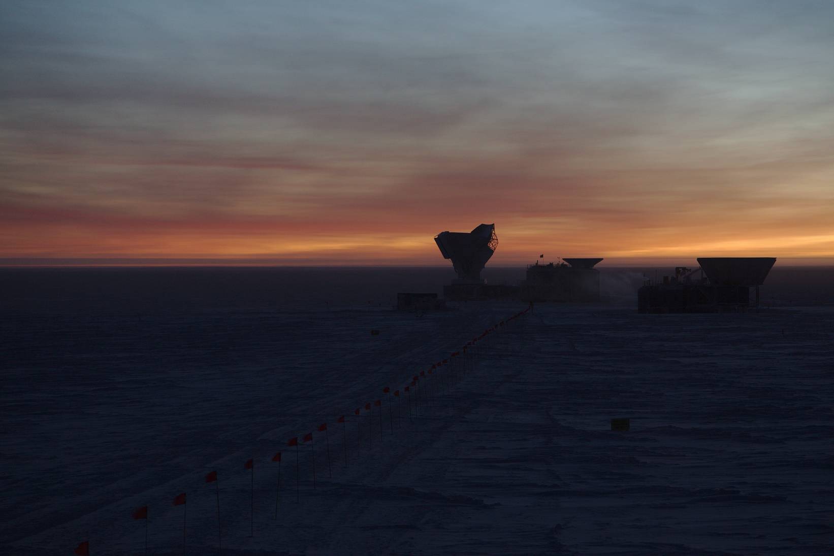 April 2017: The South Pole Telescope during EHT observations, 12 hours after the previous telescope picture. The last glimpses of the Sun behind the horizon cause the clouds in the sky to light up in hauntingly beautiful colours.
